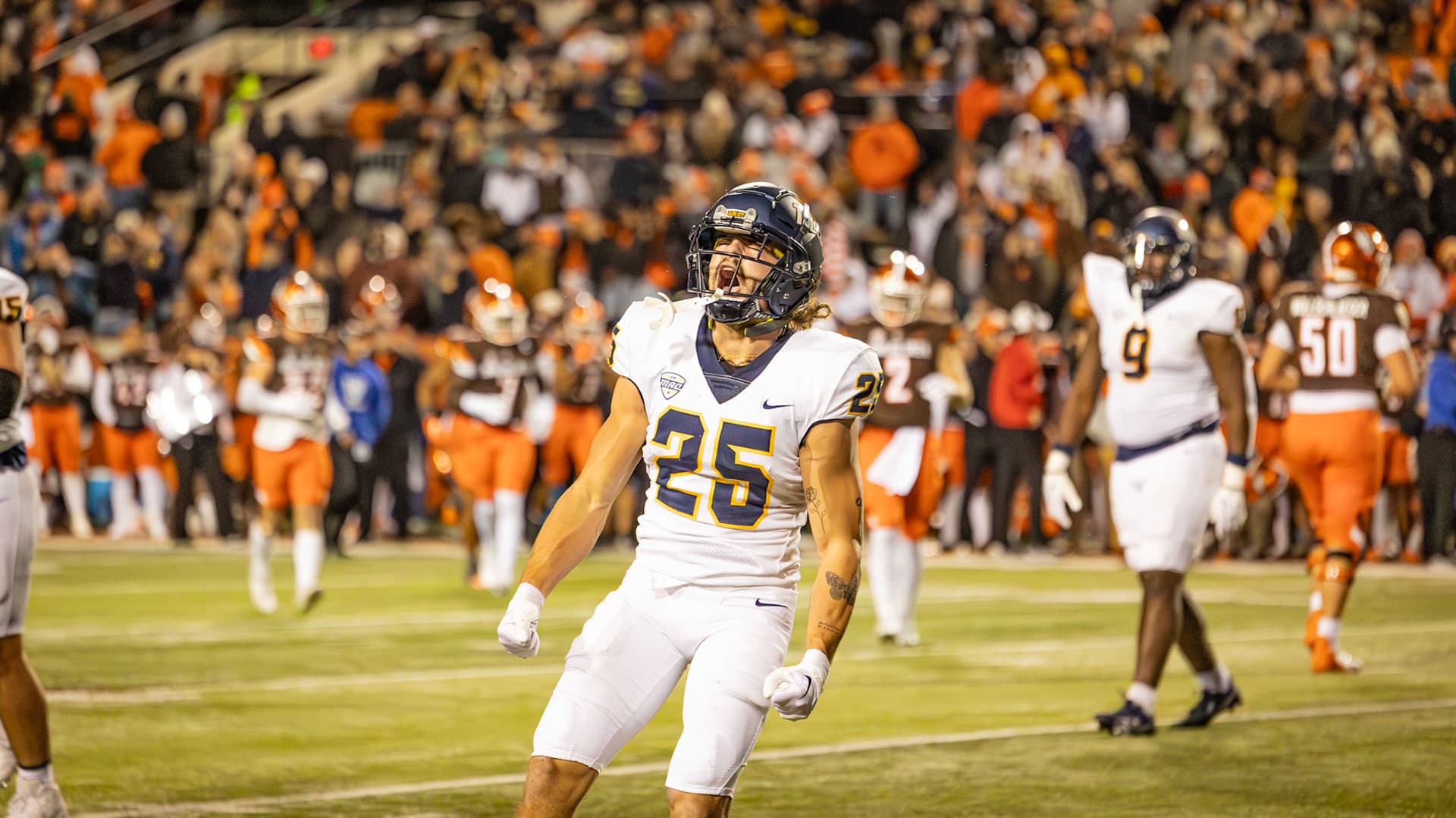 A Toledo football player celebrates on the field in front of a packed stadium crowd.