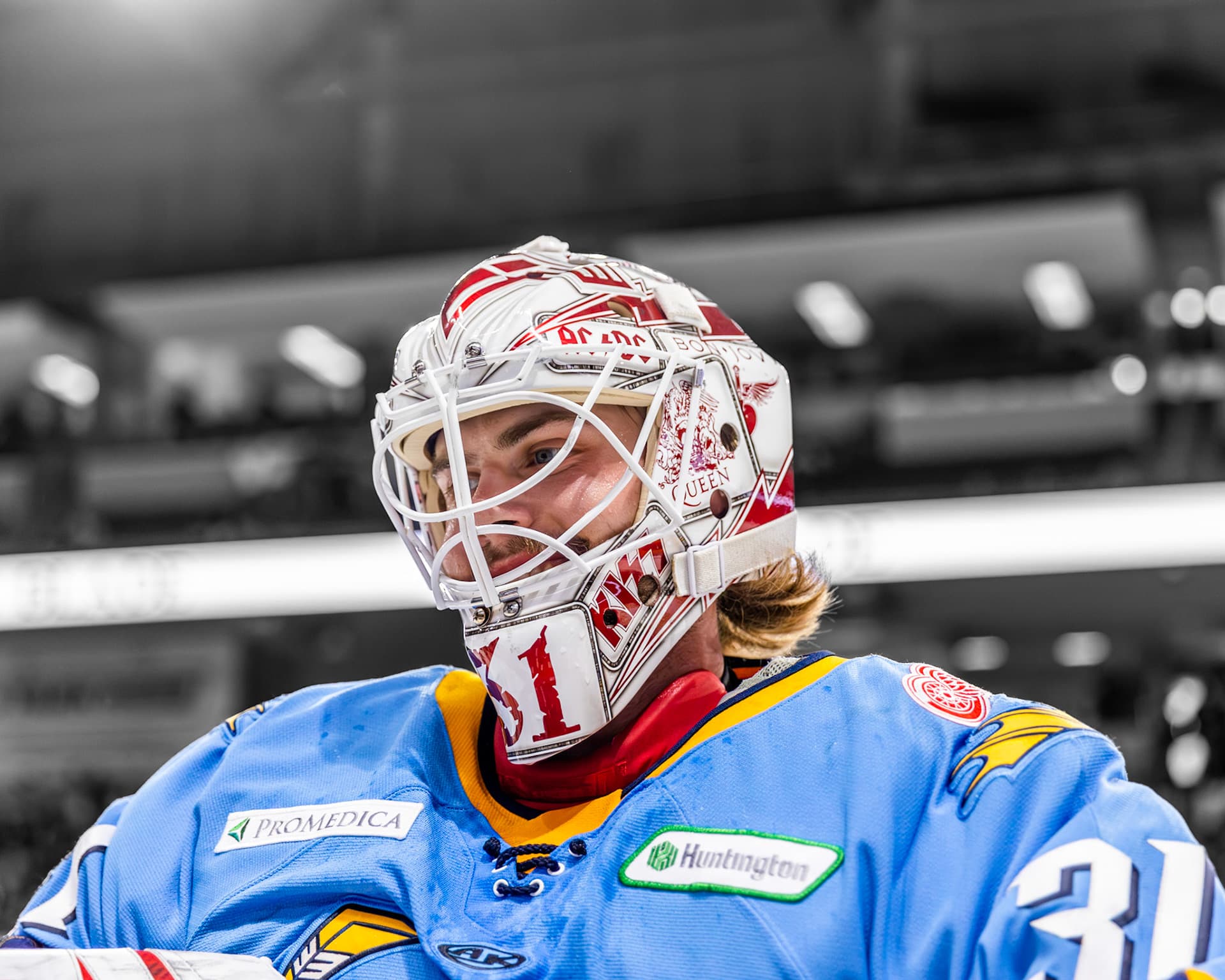 A Toledo Walleye goaltender in a red and white mask, against a black and white arena.