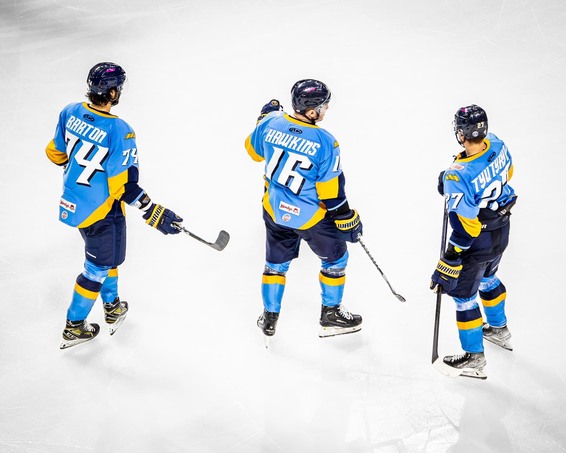Three Toledo Walleye players skate together, seen from above the ice.