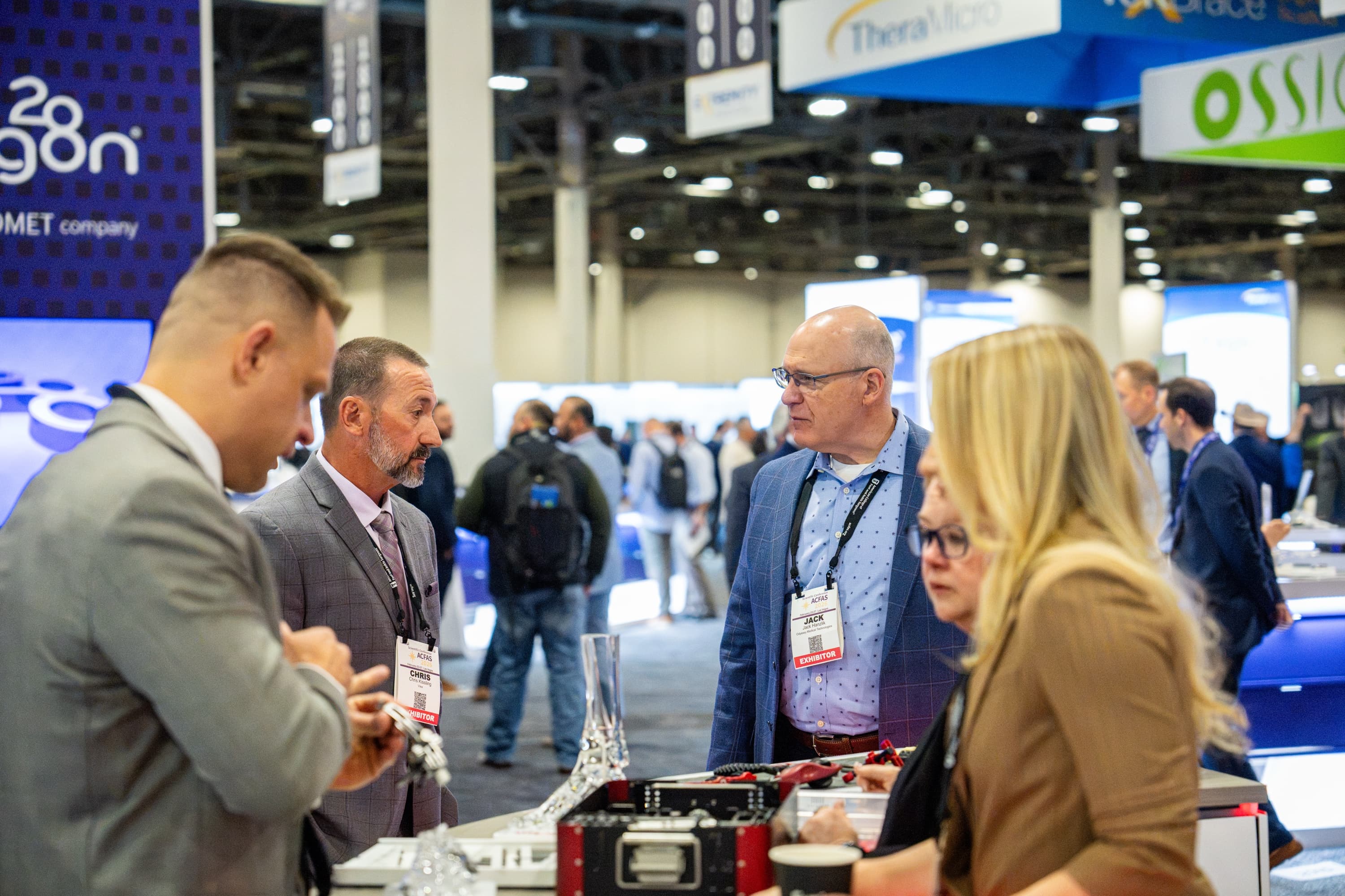 Exhibitors in conversation across a demo table on the ACFAS 2026 exhibit hall floor.